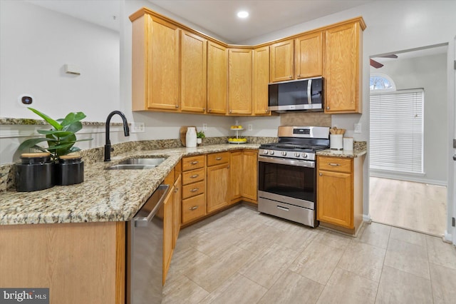 kitchen with kitchen peninsula, appliances with stainless steel finishes, light stone counters, and sink