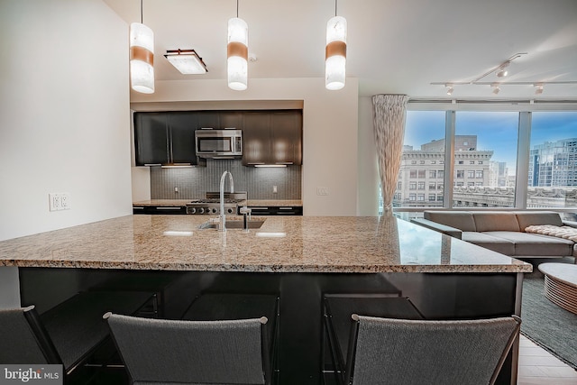 kitchen with decorative light fixtures, a kitchen bar, tasteful backsplash, sink, and light stone counters