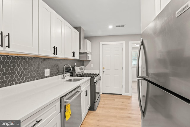 kitchen featuring white cabinets, appliances with stainless steel finishes, wall chimney exhaust hood, sink, and light hardwood / wood-style flooring