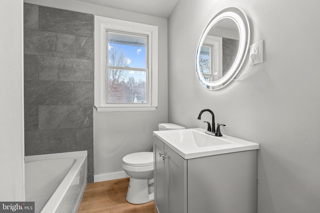 bathroom with toilet, a bath, hardwood / wood-style floors, and vanity