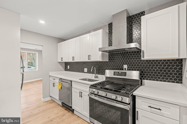 kitchen featuring sink, light wood-type flooring, appliances with stainless steel finishes, white cabinets, and wall chimney exhaust hood