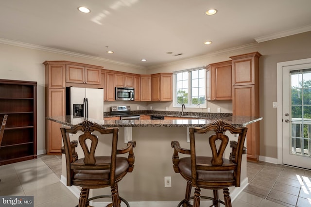 kitchen with appliances with stainless steel finishes, dark stone counters, a breakfast bar area, and a kitchen island