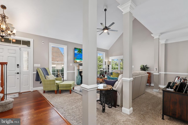 living room with ceiling fan with notable chandelier, wood-type flooring, high vaulted ceiling, and ornate columns