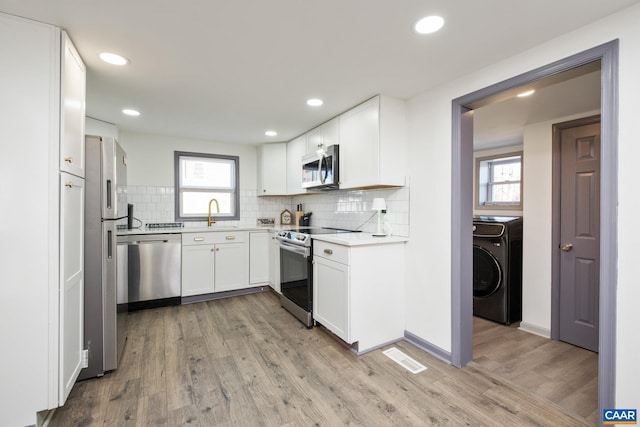 kitchen with washer / clothes dryer, white cabinetry, stainless steel appliances, light hardwood / wood-style floors, and sink