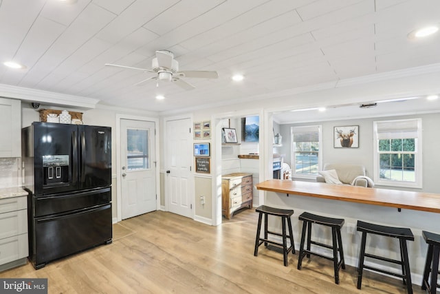 kitchen featuring black fridge, butcher block countertops, wood ceiling, ornamental molding, and a breakfast bar area