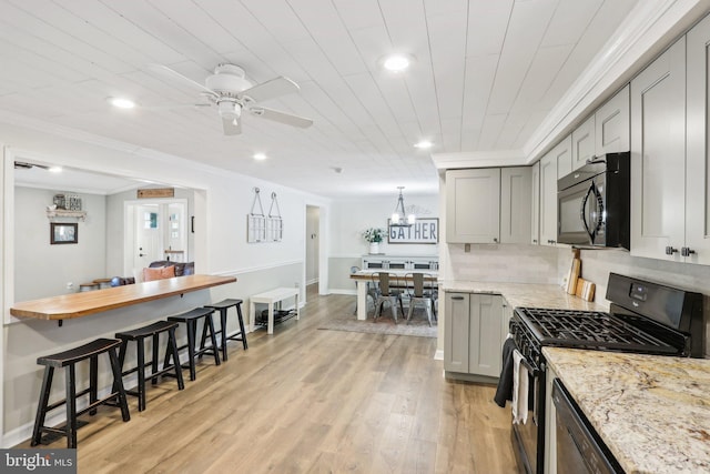 kitchen with black appliances, ornamental molding, light wood-type flooring, light stone counters, and gray cabinetry