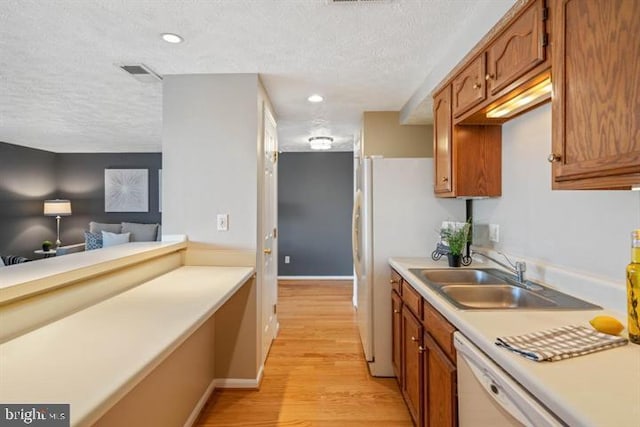 kitchen with light wood finished floors, visible vents, brown cabinets, light countertops, and a sink