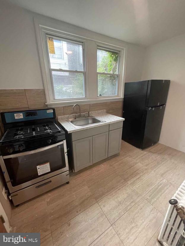 kitchen featuring gray cabinetry, sink, gas stove, and black fridge