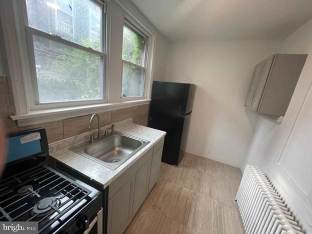 kitchen featuring tasteful backsplash, radiator, sink, and black appliances