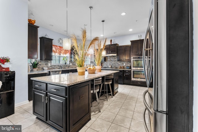 kitchen with stainless steel appliances, hanging light fixtures, a kitchen island, and light tile patterned floors