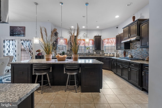 kitchen with a kitchen island, stainless steel gas cooktop, a breakfast bar area, and decorative light fixtures