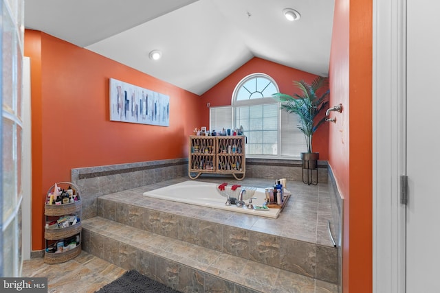 bathroom featuring lofted ceiling and tiled tub