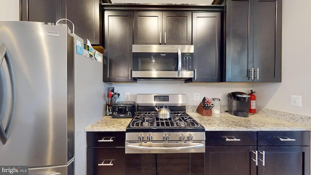 kitchen featuring dark brown cabinetry, light stone countertops, and appliances with stainless steel finishes