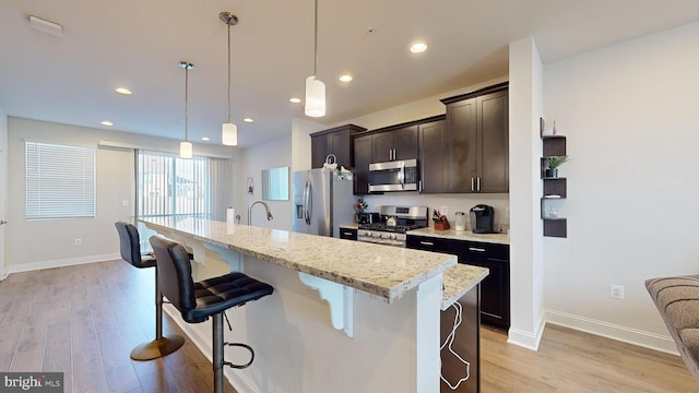 kitchen featuring appliances with stainless steel finishes, a kitchen breakfast bar, decorative light fixtures, and a kitchen island with sink