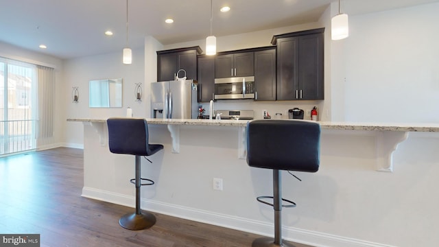 kitchen featuring appliances with stainless steel finishes, hanging light fixtures, a kitchen breakfast bar, light stone counters, and dark hardwood / wood-style flooring