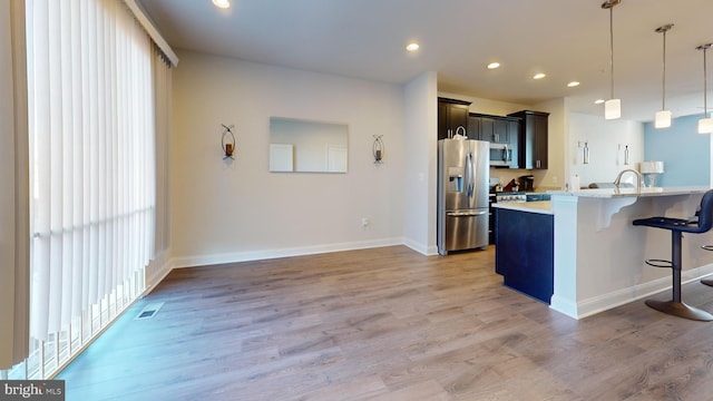 kitchen featuring a breakfast bar area, light wood-type flooring, pendant lighting, stainless steel appliances, and light stone countertops