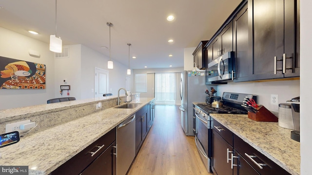 kitchen with stainless steel appliances, decorative light fixtures, light stone countertops, and sink