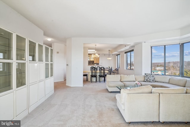 unfurnished living room featuring an inviting chandelier, baseboards, and light colored carpet