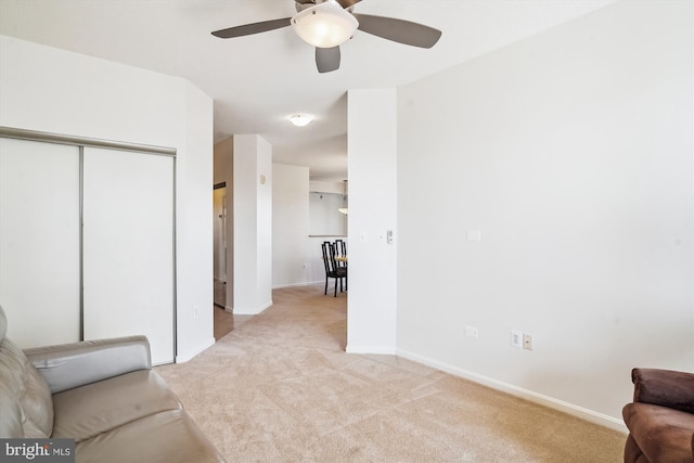 living area featuring light carpet, ceiling fan, and baseboards