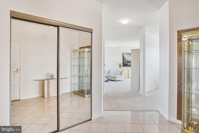 hall featuring light carpet, baseboards, and light tile patterned flooring