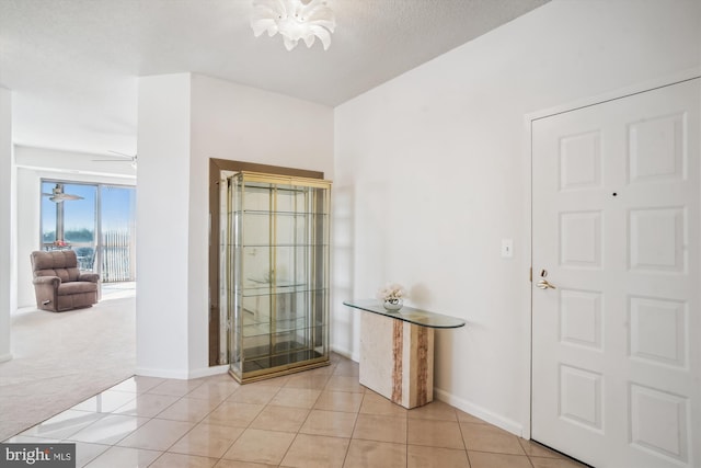 entryway with a ceiling fan, light colored carpet, light tile patterned flooring, and baseboards