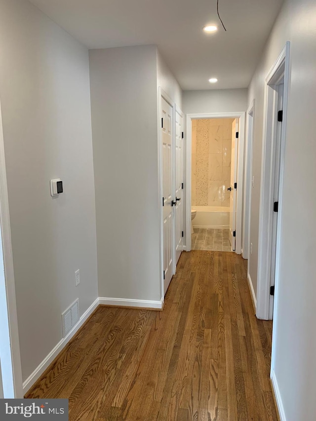 corridor featuring visible vents, baseboards, and wood finished floors