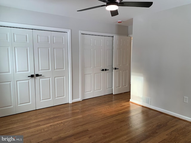 unfurnished bedroom with visible vents, two closets, baseboards, and wood finished floors