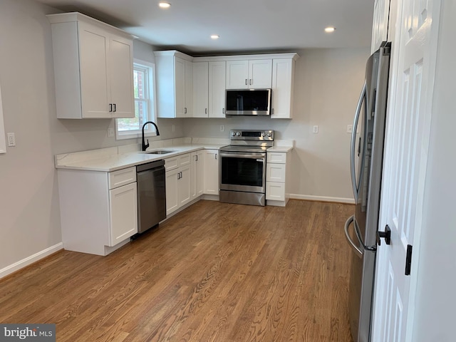 kitchen with light hardwood / wood-style floors, sink, light stone countertops, stainless steel appliances, and white cabinets