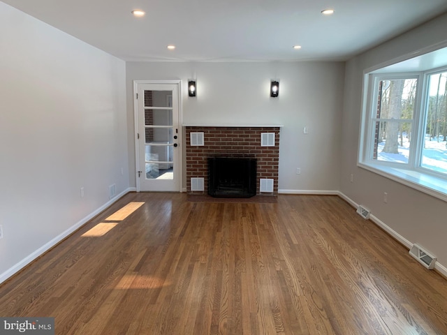 unfurnished living room with a brick fireplace, visible vents, baseboards, and wood finished floors