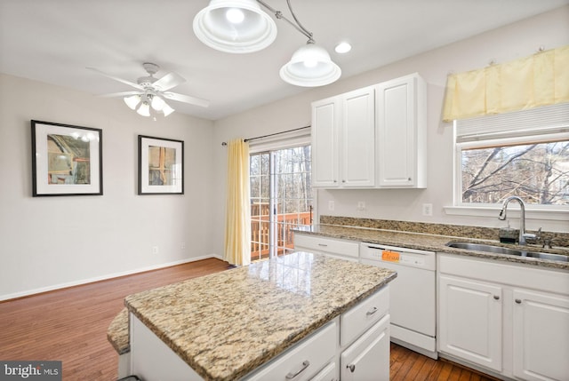 kitchen with sink, dishwasher, light stone countertops, white cabinets, and a kitchen island