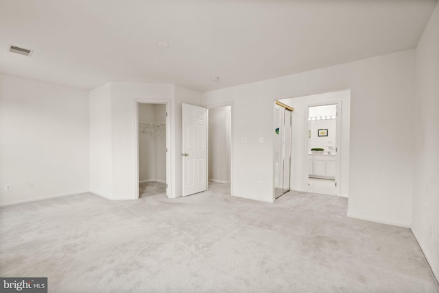 interior space with light colored carpet, connected bathroom, and a walk in closet