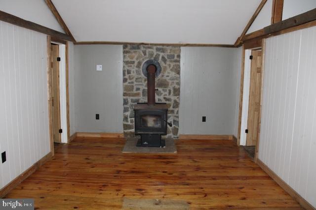 unfurnished living room with vaulted ceiling with beams, a wood stove, and hardwood / wood-style flooring