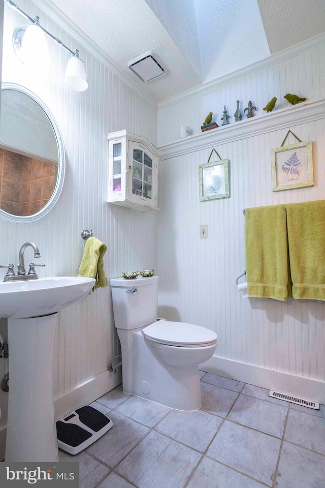 bathroom with a textured ceiling, tile patterned floors, wooden walls, toilet, and crown molding