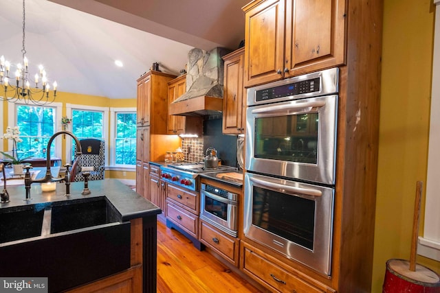 kitchen featuring lofted ceiling, backsplash, custom exhaust hood, an inviting chandelier, and appliances with stainless steel finishes