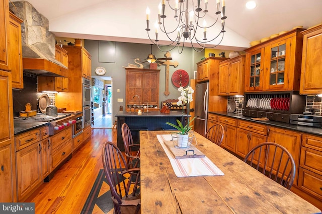 kitchen featuring appliances with stainless steel finishes, decorative backsplash, a notable chandelier, vaulted ceiling, and pendant lighting