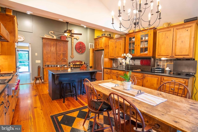 kitchen featuring ceiling fan with notable chandelier, stainless steel appliances, an island with sink, tasteful backsplash, and a kitchen breakfast bar