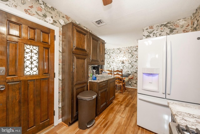 kitchen featuring ceiling fan, light stone countertops, white refrigerator with ice dispenser, and light hardwood / wood-style flooring