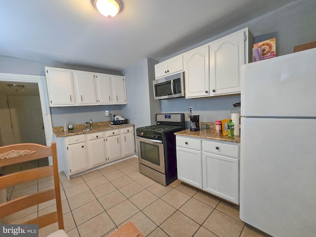 kitchen with light tile patterned floors, appliances with stainless steel finishes, white cabinets, and light stone countertops