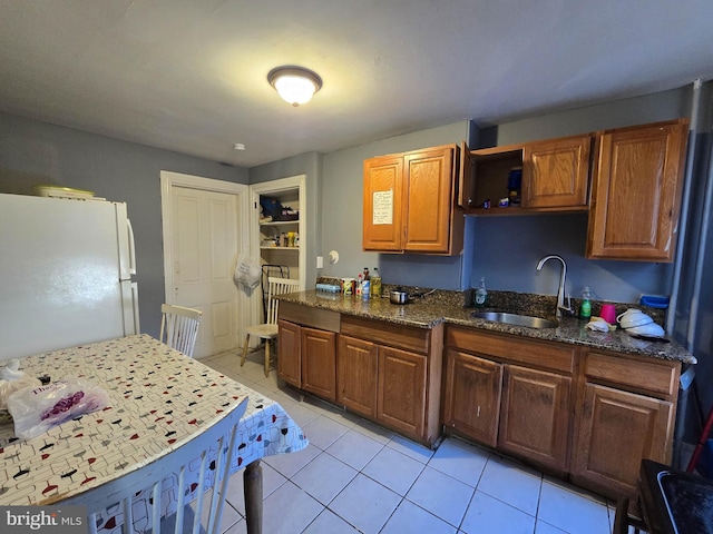 kitchen featuring light tile patterned floors, dark stone counters, sink, and white fridge