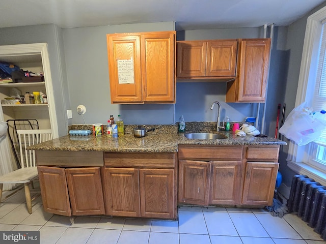 kitchen with sink, dark stone countertops, radiator, and light tile patterned flooring