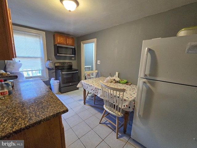 kitchen featuring light tile patterned floors, appliances with stainless steel finishes, and dark stone countertops