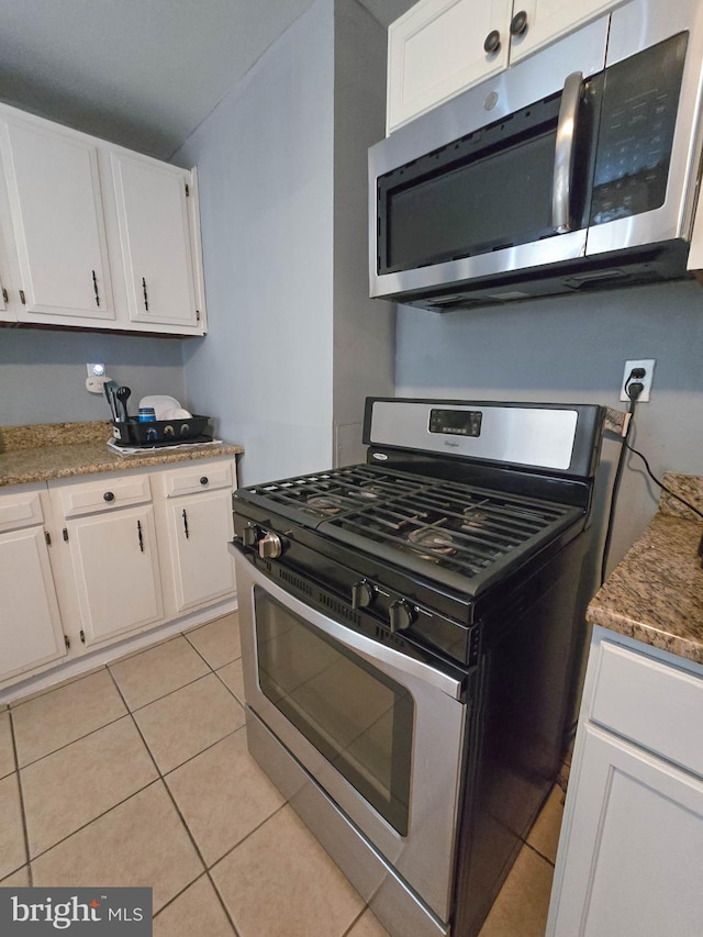 kitchen with light tile patterned floors, stone countertops, stainless steel appliances, and white cabinetry