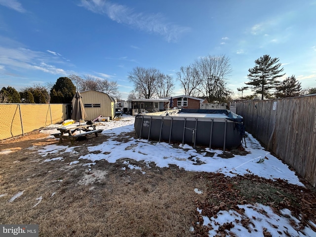 yard covered in snow featuring a fenced in pool and a storage unit