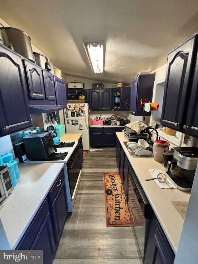 kitchen featuring black gas range oven, blue cabinetry, white fridge, and lofted ceiling