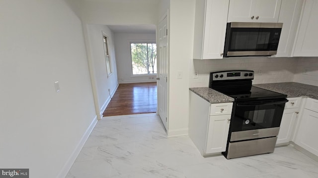 kitchen featuring decorative backsplash, white cabinetry, stainless steel appliances, and dark stone countertops