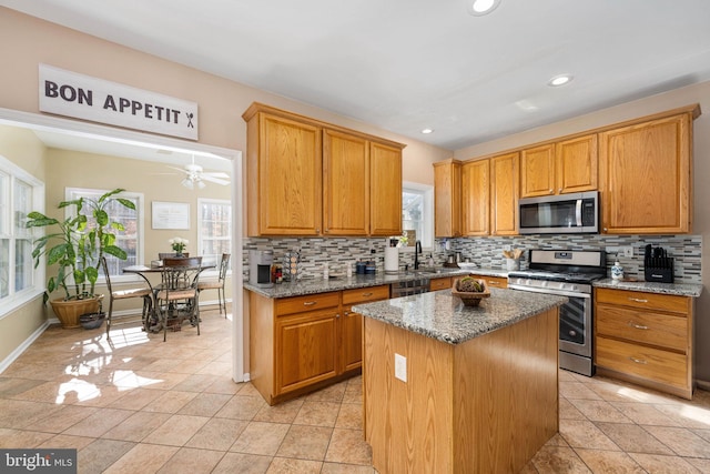 kitchen featuring appliances with stainless steel finishes, a center island, dark stone counters, backsplash, and ceiling fan