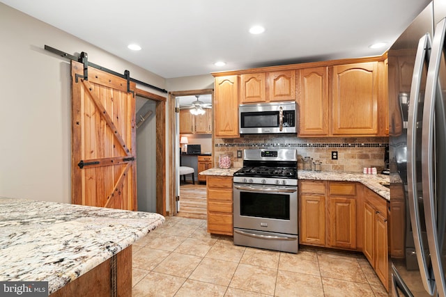 kitchen with light stone counters, appliances with stainless steel finishes, a barn door, and tasteful backsplash