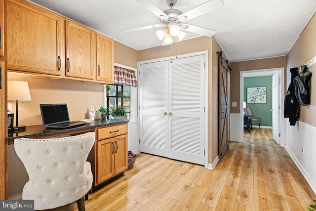 kitchen with ceiling fan, light hardwood / wood-style flooring, a barn door, and a textured ceiling