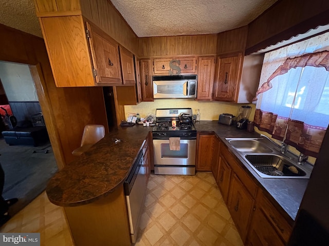 kitchen featuring kitchen peninsula, sink, wooden walls, stainless steel appliances, and a textured ceiling