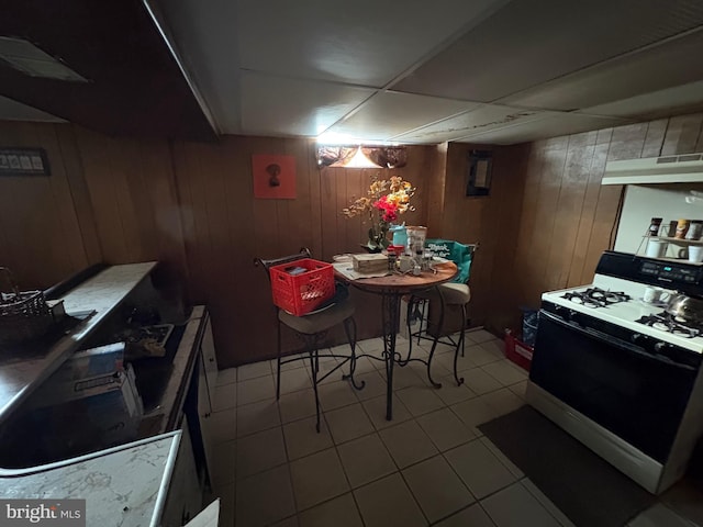 kitchen with light tile patterned floors, a drop ceiling, gas range oven, and wood walls